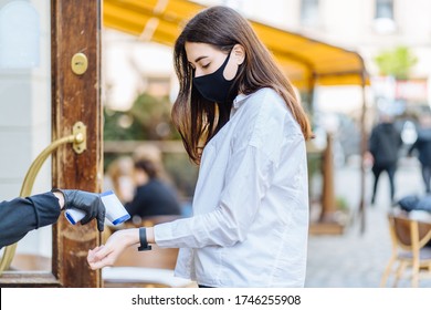 Young brunette woman customer in facial mask coming in a cafe and getting her temperature measured with infrared thermometer. Concept of a new social rules after coronavirus pandemic - Powered by Shutterstock