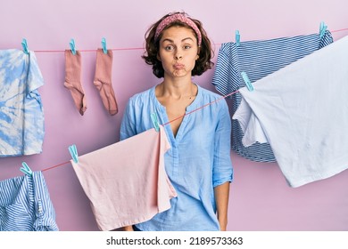 Young brunette woman doing laundry around string hangs puffing cheeks with funny face. mouth inflated with air, crazy expression. 