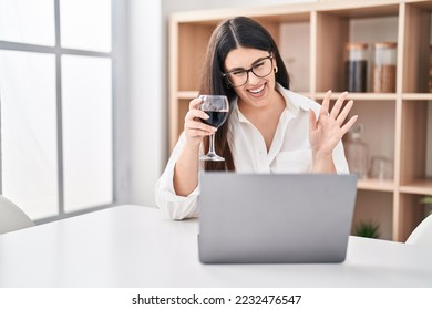 Young brunette woman doing video call with laptop drinking a glass of wine looking positive and happy standing and smiling with a confident smile showing teeth  - Shutterstock ID 2232476547