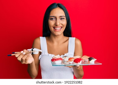 Young brunette woman eating butterfish sushi using chopsticks smiling and laughing hard out loud because funny crazy joke. 