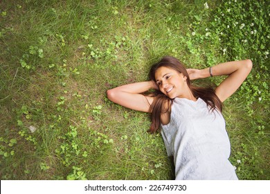 Junge Brunette-Frau, die das Liegen auf dem Rücken auf dem grünen Gras im Garten genießt. Draufsicht.