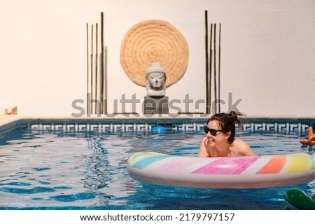 Young brunette woman enjoying the summer at the swimming pool with a mat and wearing sunglasses