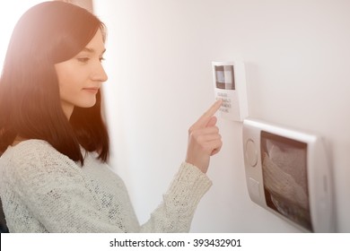 Young brunette woman entering code on keypad of home security alarm. Video intercom next to alarm keypad.