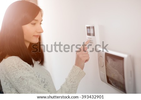 Young brunette woman entering code on keypad of home security alarm. Video intercom next to alarm keypad.