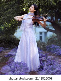 Young brunette woman in fairy violet dress playing th violin among lavender flowers
