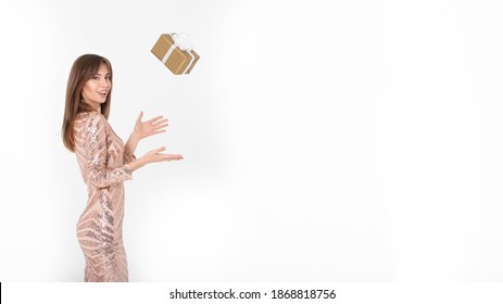 A Young Brunette Woman In A Festive Dress Catches A Box With A Gift On A White Background. Soft Focus. Christmas And New Year Celebration Concept. Isolated On White With Copy Space.