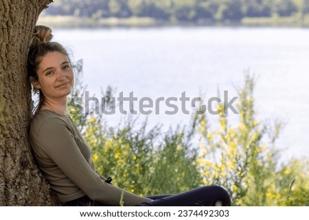 A young brunette woman finds solace in the lush green forest, gazing upon a tranquil blue lake, embracing the serenity of a summer's day. Serene Forest Lake Meditation. High quality photo