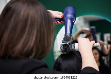 Young Brunette Woman Getting Ready For Party. Professional Hairdresser Making Hairstyling For Female Client With Hair Dryer In Front Of Big Mirror. Close-up Picture Of Work Process In Barber Shop.