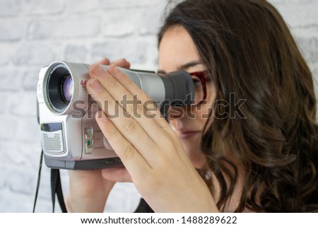 Young brunette woman with glasses holding an old retro video camcorder camera