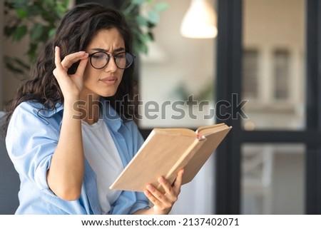 Young brunette woman in glasses reading book, having poor eyesight at home, copy space. Millennial female student experiencing problem with vision or eye fatigue, doing homework with textbook