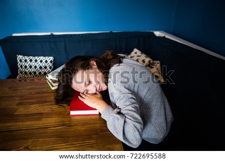 Young brunette woman in a grey sweater fell asleep in the book from fatigue