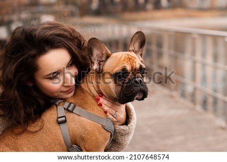 Young brunette woman with her pet french bulldog walking in park, lifestyle, autumn fall season