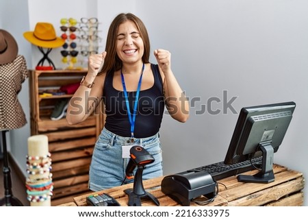 Young brunette woman holding banner with open text at retail shop excited for success with arms raised and eyes closed celebrating victory smiling. winner concept. 