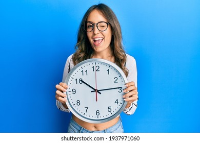 Young Brunette Woman Holding Big Clock Winking Looking At The Camera With Sexy Expression, Cheerful And Happy Face. 