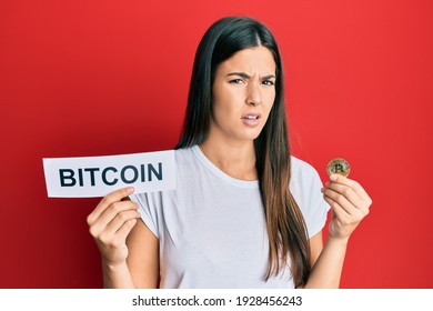 Young Brunette Woman Holding Bitcoin Virtual Money Clueless And Confused Expression. Doubt Concept. 