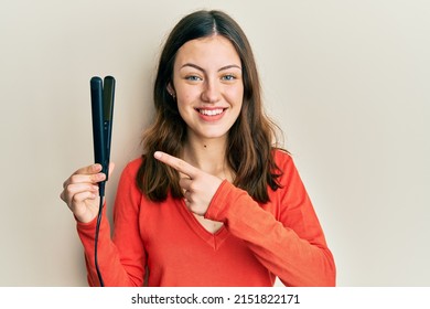 Young Brunette Woman Holding Hair Straightener Smiling Happy Pointing With Hand And Finger 