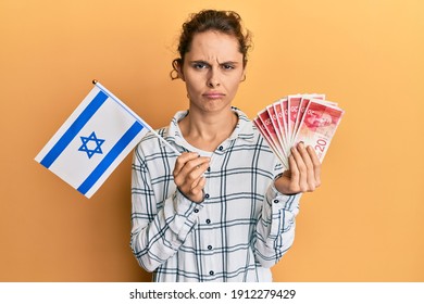 Young Brunette Woman Holding Israel Flag And Shekels Banknotes Depressed And Worry For Distress, Crying Angry And Afraid. Sad Expression. 