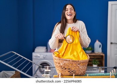 Young brunette woman holding magnifying glass looking for stain at clothes smiling and laughing hard out loud because funny crazy joke. 