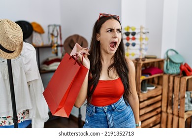 Young Brunette Woman Holding Shopping Bags At Retail Shop Angry And Mad Screaming Frustrated And Furious, Shouting With Anger. Rage And Aggressive Concept. 