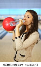 Young Brunette Woman Holds Red Ball And Drinks Pure Water From Bottle In Bowling Club; Shallow Depth Of Field