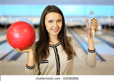 Young Brunette Woman Holds Red Ball And Bottle With Water In Bowling Club; Shallow Depth Of Field