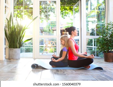 Young brunette woman with little daughter in a sporty uniform doing yoga on the terrace of a house by the garden - Powered by Shutterstock