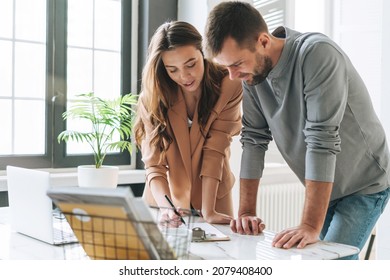 Young brunette woman with long hair in stylish suit working with young man using at laptop on table with green house plant in the bright modern office - Shutterstock ID 2079408400