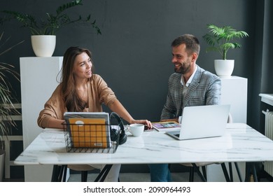 Young Brunette Woman With Long Hair In The Stylish Suit Working With Young Man Using Laptop On Table With Green House Plant In Bright Modern Office, Team Work