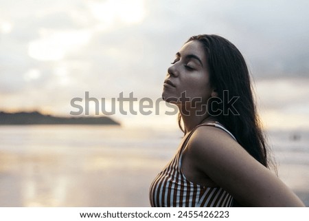 Young brunette woman with long hair standing on a beautiful beach in Costa Rica, watching the sunset