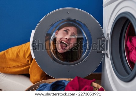 Young brunette woman looking through the washing machine window angry and mad screaming frustrated and furious, shouting with anger looking up. 