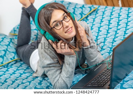 a young brunette woman lying on the bed listening to music