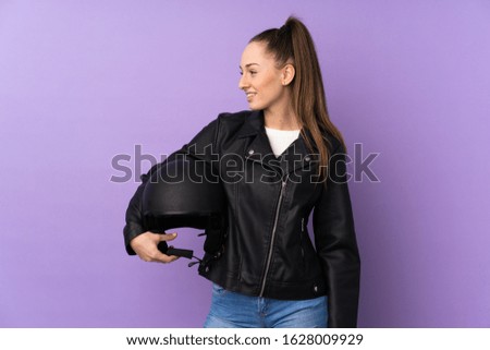 Young brunette woman with a motorcycle helmet over isolated purple background with happy expression