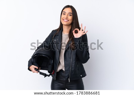 Young brunette woman with a motorcycle helmet over isolated white background showing ok sign with fingers