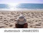 Young brunette woman on her back sunbathing alone with her pretty hat in front of the blue sea at sunset on a summer vacation day