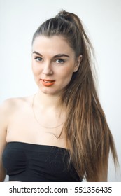 Young Brunette Woman On A White Background. Woman Orange Lips. Portrait Of Beauty Girl. A Girl From A High Ponytail Long Hair. She Is Smilling.