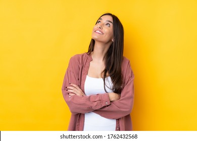 Young brunette woman over isolated yellow background looking up while smiling