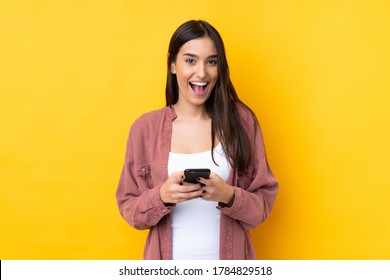 Junge brunettenreiche Frau auf einzeln gelbem Hintergrund überrascht und sendet eine Nachricht