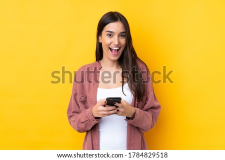 Young brunette woman over isolated yellow background surprised and sending a message