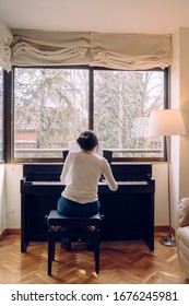 Young brunette woman playing the piano at home. Isolated woman pianist composing a new classical song. Teacher pianist musician rehearsing classical music. Professional musician lifestyles indoors.