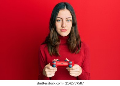 Young Brunette Woman Playing Video Game Holding Controller Relaxed With Serious Expression On Face. Simple And Natural Looking At The Camera. 