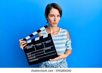 Young Brunette Woman With Short Hair Holding Video Film Clapboard Clueless And Confused Expression. Doubt Concept. 