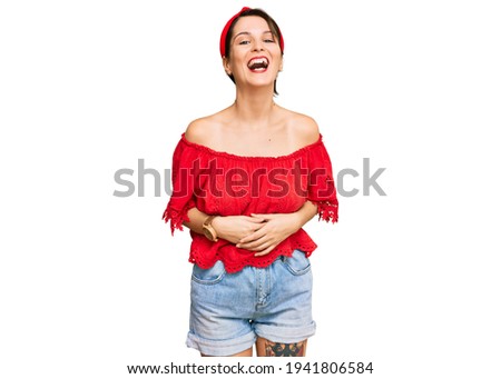 Young brunette woman with short hair wearing casual summer clothes and diadem smiling and laughing hard out loud because funny crazy joke with hands on body. 