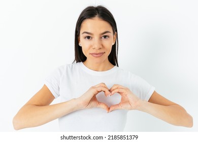 Young Brunette Woman Showing Heart Symbol With Fingers Holding Hands Near Chest, Standing On White Studio Background