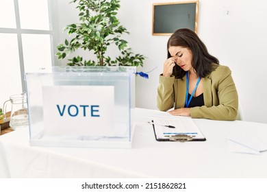 Young Brunette Woman Sitting At Election Table With Voting Ballot Tired Rubbing Nose And Eyes Feeling Fatigue And Headache. Stress And Frustration Concept. 