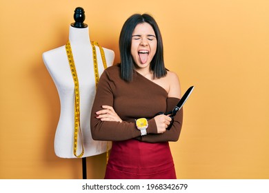 Young Brunette Woman Standing By Manikin Holding Scissors Sticking Tongue Out Happy With Funny Expression. 