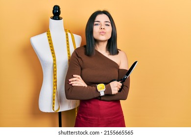 Young Brunette Woman Standing By Manikin Holding Scissors Looking At The Camera Blowing A Kiss Being Lovely And Sexy. Love Expression. 