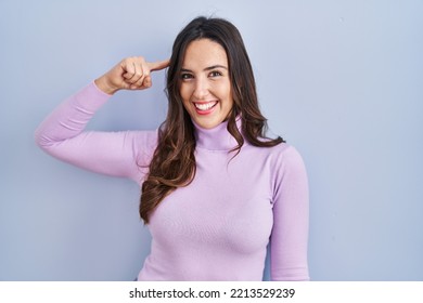 Young Brunette Woman Standing Over Blue Background Smiling Pointing To Head With One Finger, Great Idea Or Thought, Good Memory 