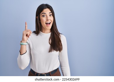 Young brunette woman standing over blue background pointing finger up with successful idea. exited and happy. number one.  - Shutterstock ID 2254302699