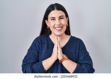 Young brunette woman standing over isolated background praying with hands together asking for forgiveness smiling confident.  - Shutterstock ID 2255668925