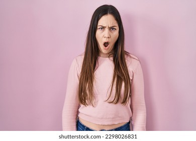 Young brunette woman standing over pink background in shock face, looking skeptical and sarcastic, surprised with open mouth  - Shutterstock ID 2298026831